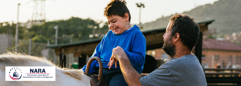 A happy young boy riding a pony with the help of a recreational therapist