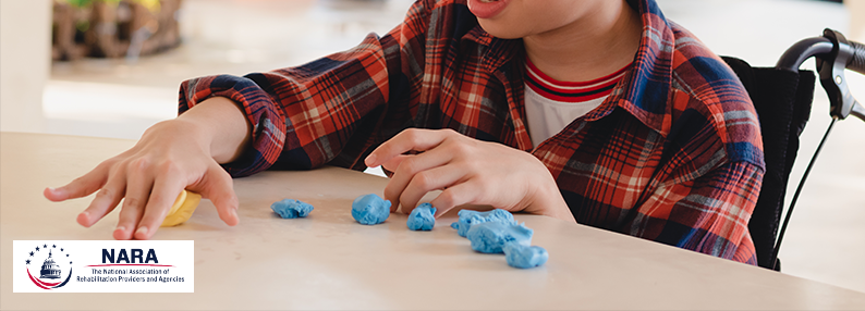  Child in wheelchair playing with playdough.