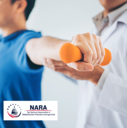 Person with arms stretched out on either side holding weights with physical therapist standing by them