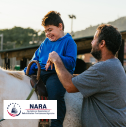 A happy young boy riding a pony with the help of a recreational therapist