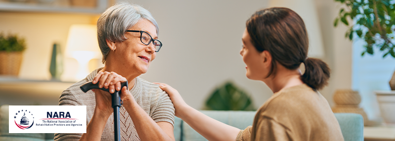 Younger woman smiling at older woman who is smiling back and has her hands on a cane