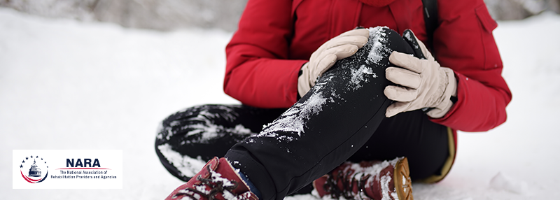 Someone wearing snow gear and sitting in the snow holding their knee