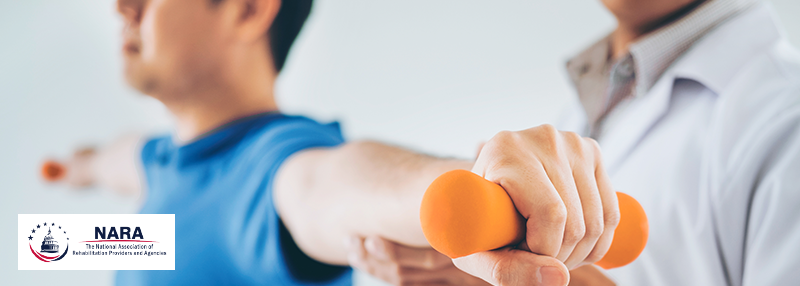 Person with arms stretched out on either side holding weights with physical therapist standing by them